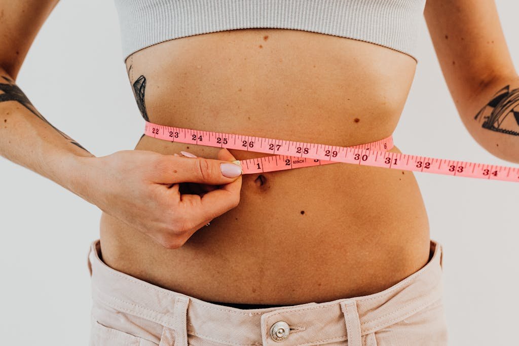 A woman measuring her waist with a pink measuring tape, focusing on fitness and health.